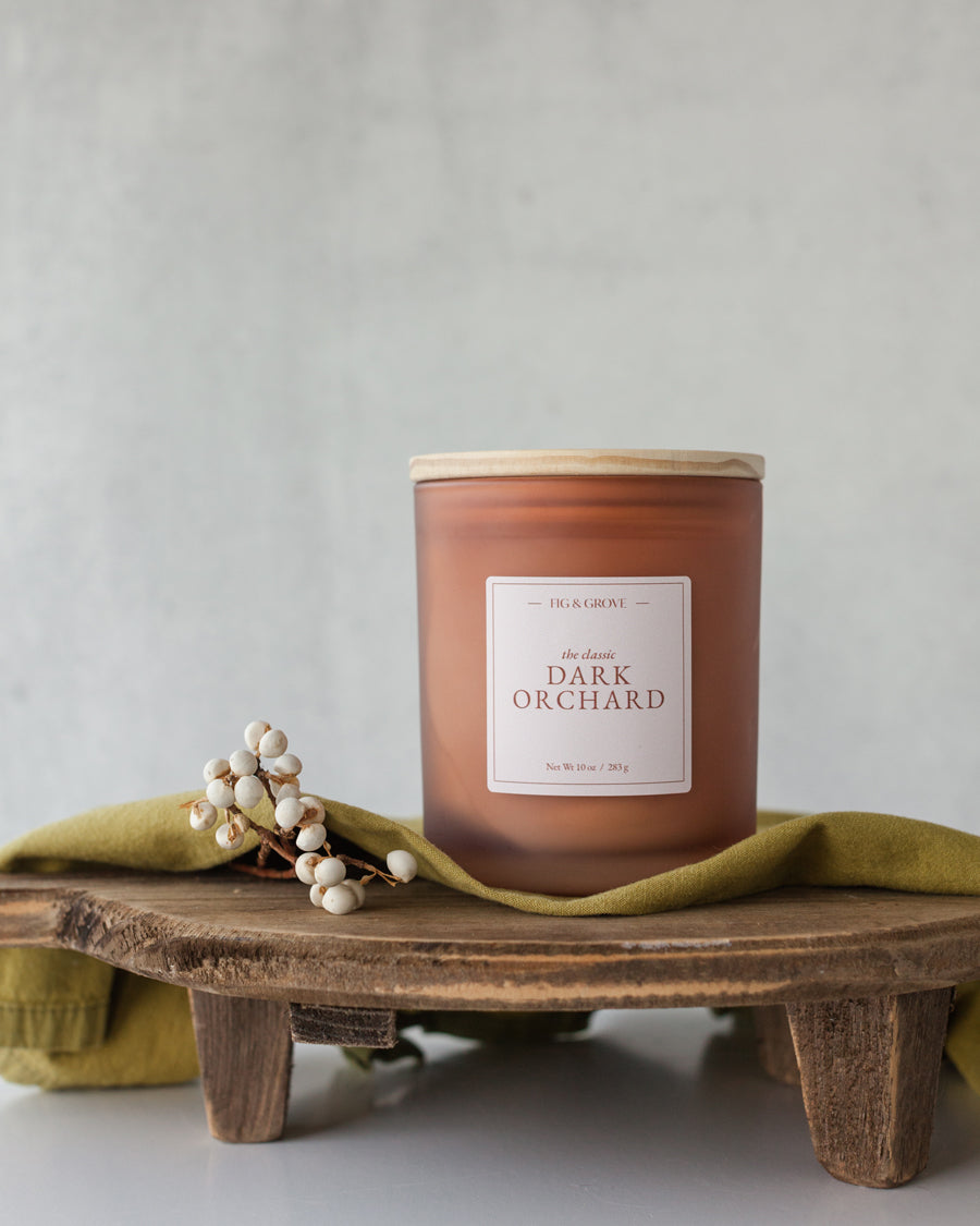 Dark Orchard candle in amber glass jar on dark wood surface, evoking cherries, spice, and candlelight – Fig &amp; Grove