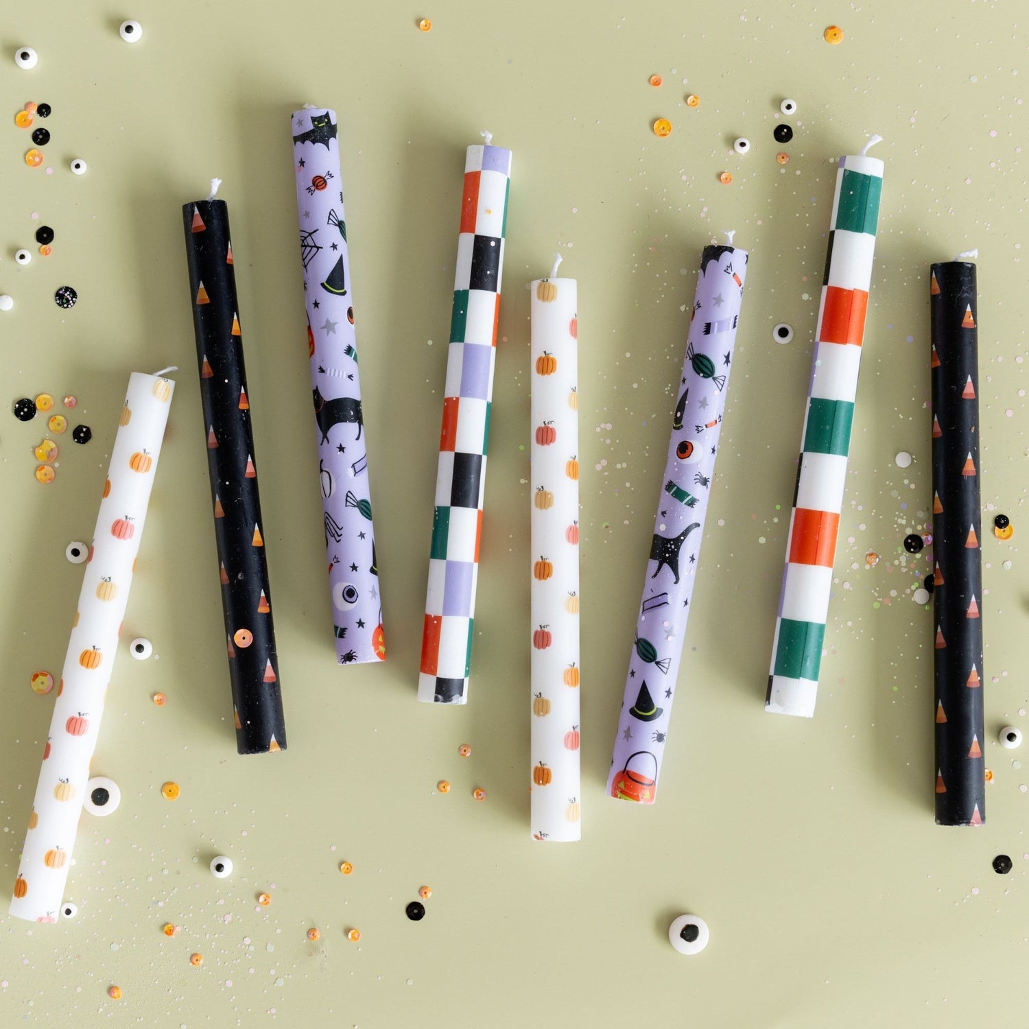 Assorted Halloween taper candles in checkered and printed patterns on green with confetti.