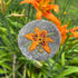 Embroidered day lily design on a textured gray surface with orange daylily in the background