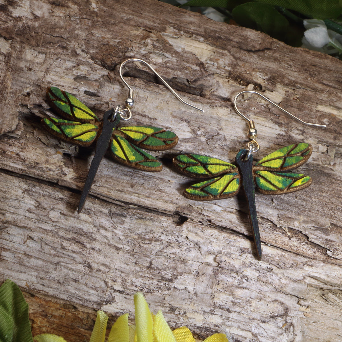 Dragonfly-shaped earrings on a wooden surface with green leaves.