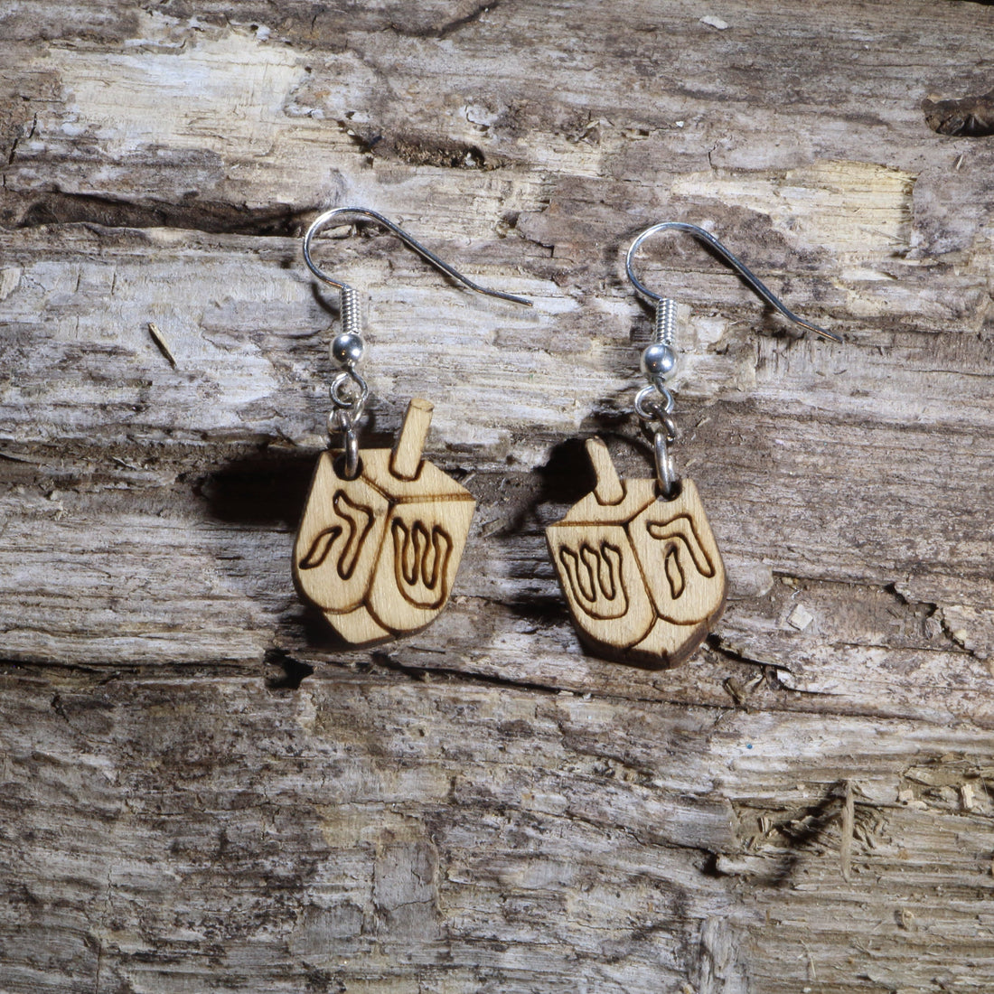Hand-painted wooden dreidel dangle earrings featuring traditional Hanukkah spinning tops engraved with classic Hebrew letters. Crafted from lightweight wood with hypoallergenic .925 sterling silver hooks, these festive earrings are perfect for Hanukkah celebrations, Jewish holidays, synagogue events, cultural festivals, meaningful holiday gifts, and anyone who loves faith-inspired seasonal jewelry.