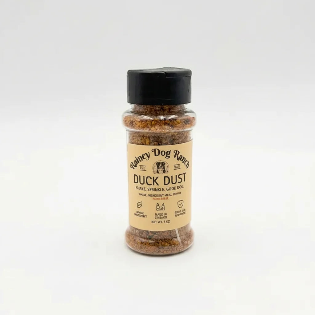 A small clear plastic bottle of Rainey Dog Ranch Duck Dust seasoning with a black cap and a tan label, centered on a light gray background.