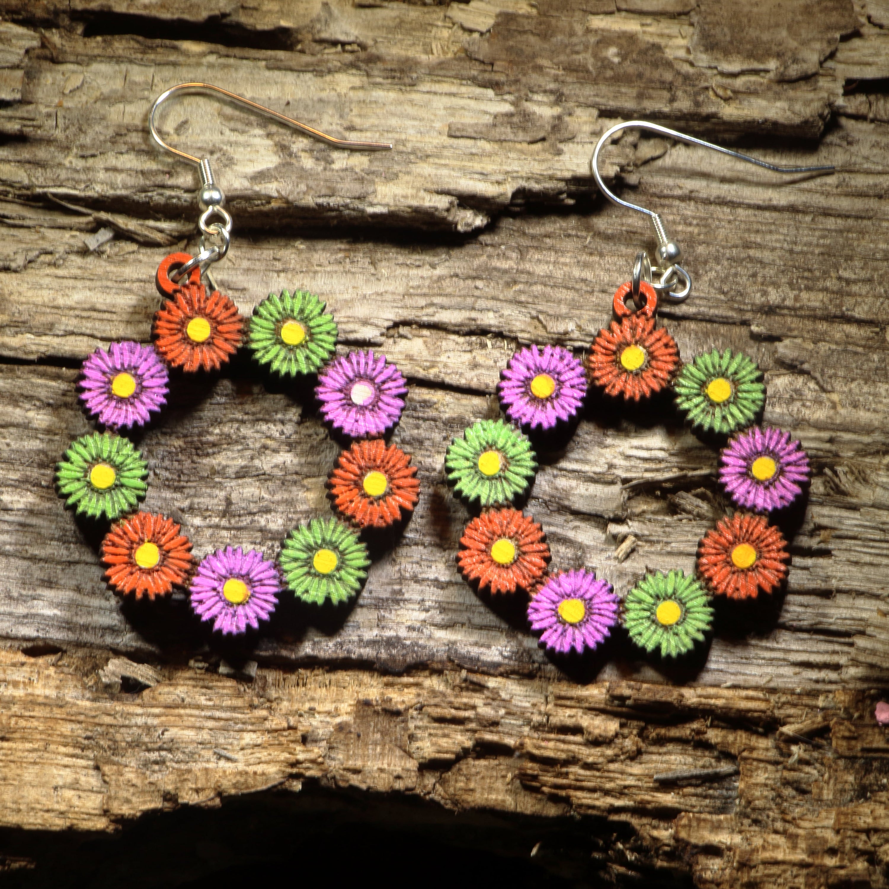 Hand-painted wooden floral daisy hoop dangle earrings featuring a delicate circular wreath of blooming daisies with cheerful spring-inspired details. Crafted from lightweight wood with hypoallergenic .925 sterling silver hooks, these artisan earrings are perfect for flower lovers, spring fashion, cottagecore style, garden enthusiasts, botanical jewelry collectors, and anyone who enjoys bright floral accessories inspired by nature.
