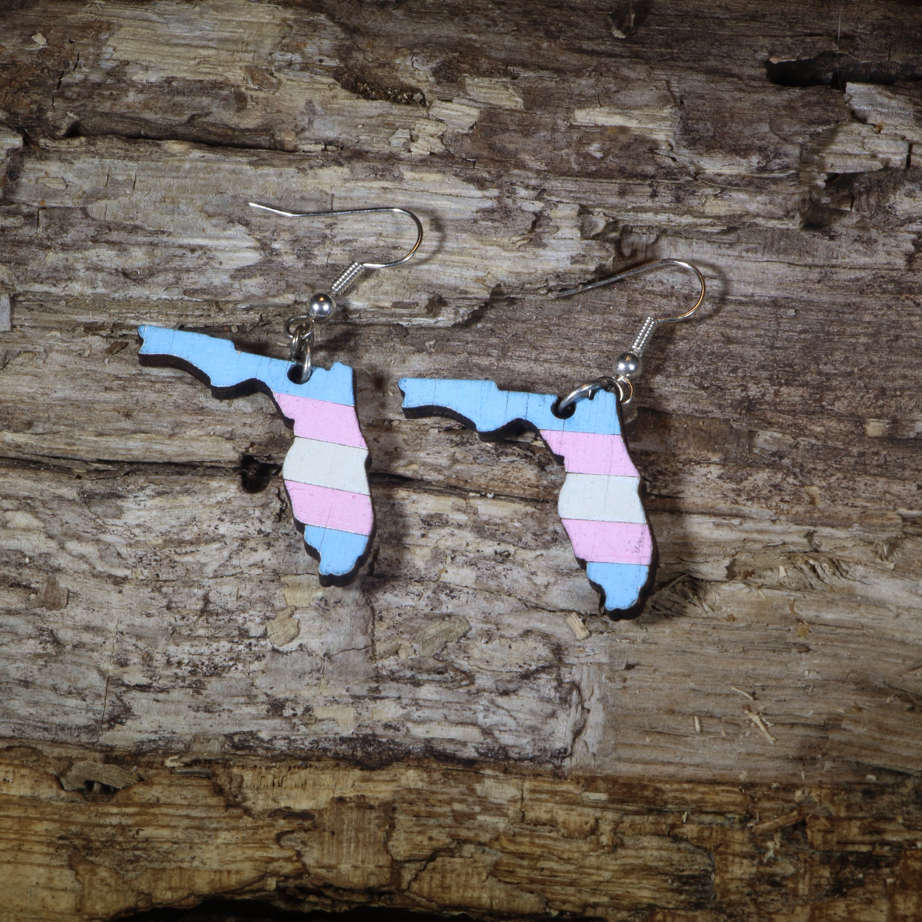 Hand-painted wooden Florida transgender pride dangle earrings featuring the Florida state silhouette with pink, blue, and white transgender pride stripes, hypoallergenic sterling silver hooks, and lightweight LGBTQ+ state pride jewelry by Cate&