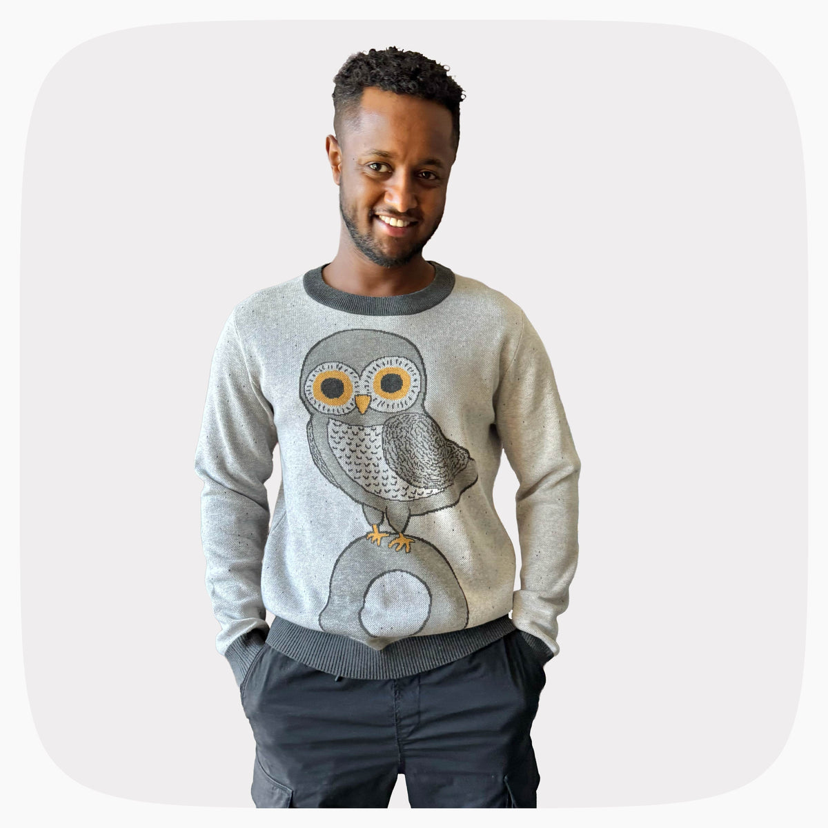 A man wearing a gray graphic knit sweater with an owl standing on the letter O design.