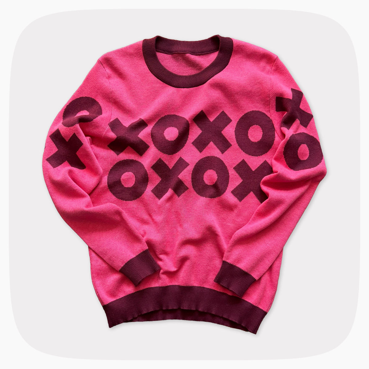 A pink graphic knit sweater with a dark red XOXO pattern across the chest.