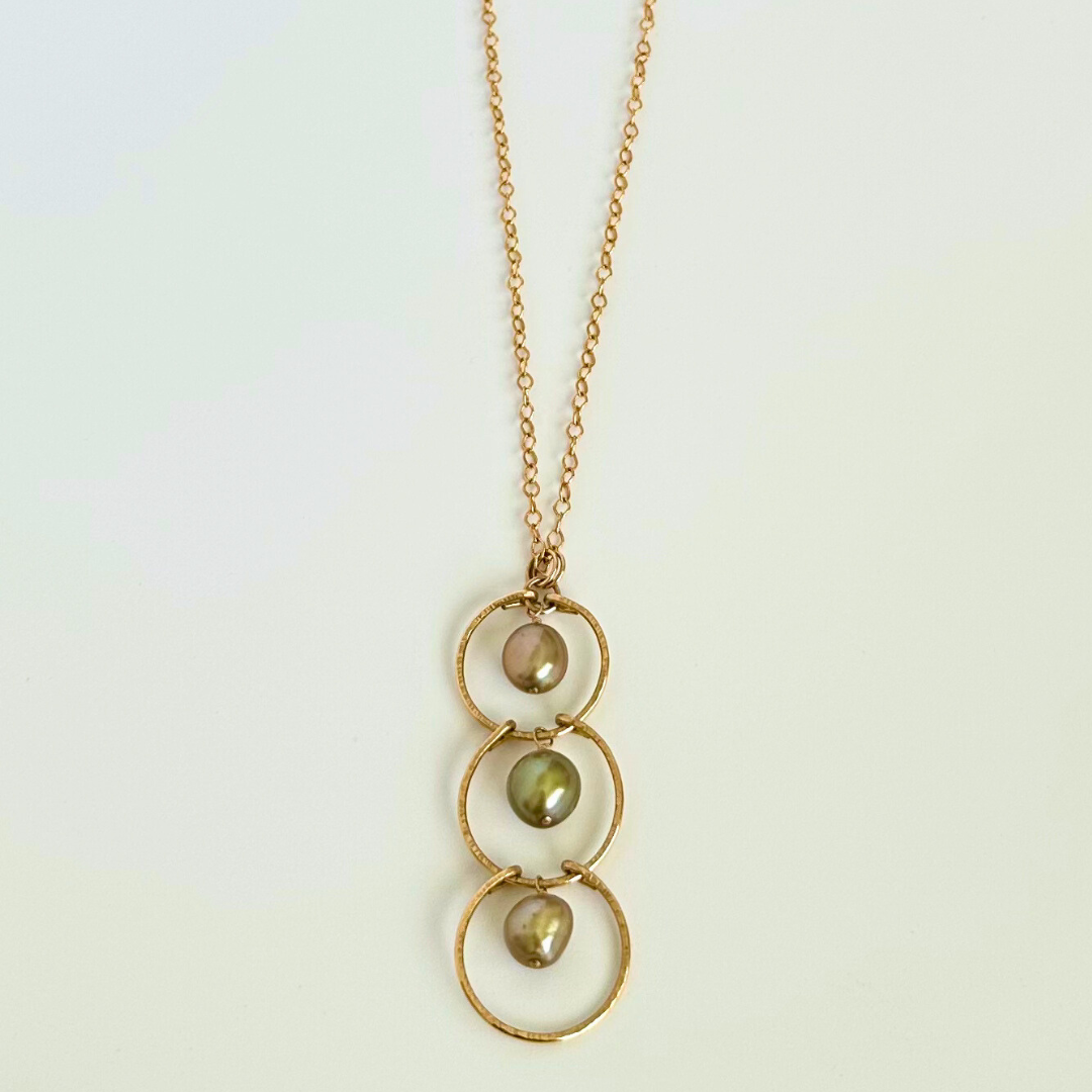 Gold necklace with three circular pendants and green pearls on a light background