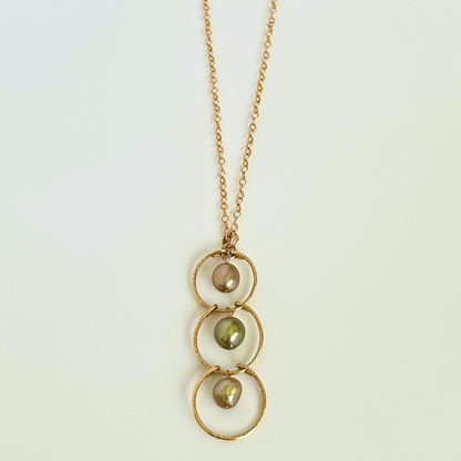 Gold necklace with three circular pendants and green pearls on a light background