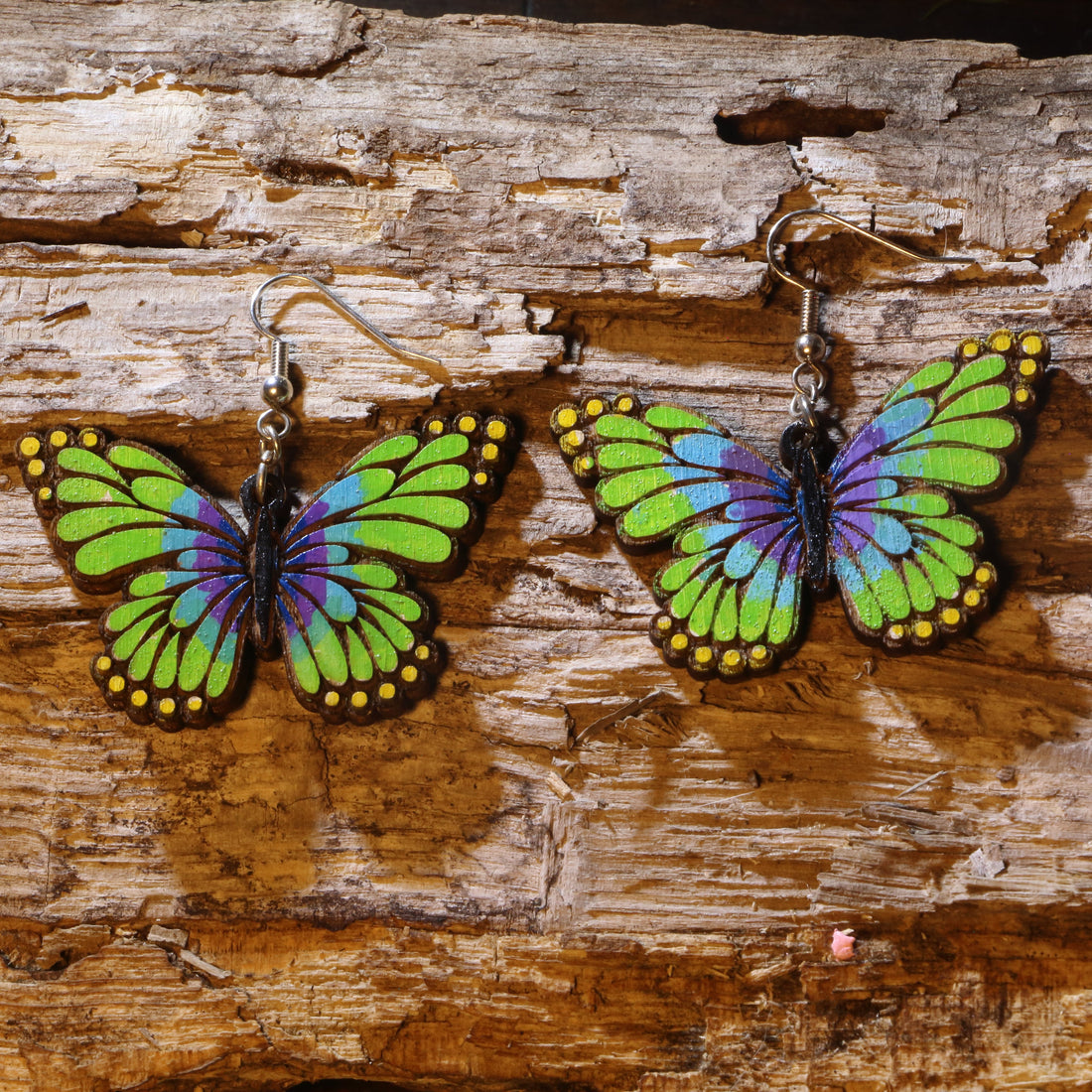 Hand-painted wooden green and purple butterfly dangle earrings featuring vibrant butterfly wings with bold nature-inspired colors. Lightweight butterfly earrings with hypoallergenic .925 sterling silver hooks, perfect for butterfly lovers, gardeners, spring fashion, nature enthusiasts, and anyone who enjoys colorful botanical-inspired jewelry.