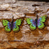 Hand-painted wooden green and purple butterfly dangle earrings featuring vibrant butterfly wings with bold nature-inspired colors. Lightweight butterfly earrings with hypoallergenic .925 sterling silver hooks, perfect for butterfly lovers, gardeners, spring fashion, nature enthusiasts, and anyone who enjoys colorful botanical-inspired jewelry.