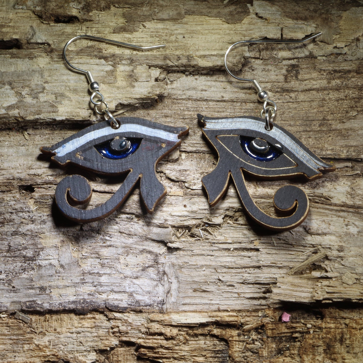 Hand-painted Eye of Horus wooden dangle earrings featuring the iconic ancient Egyptian symbol with bold black, silver, and blue details. Lightweight Egyptian jewelry perfect for history lovers, mythology enthusiasts, Egyptology fans, and anyone drawn to ancient Egyptian symbols.