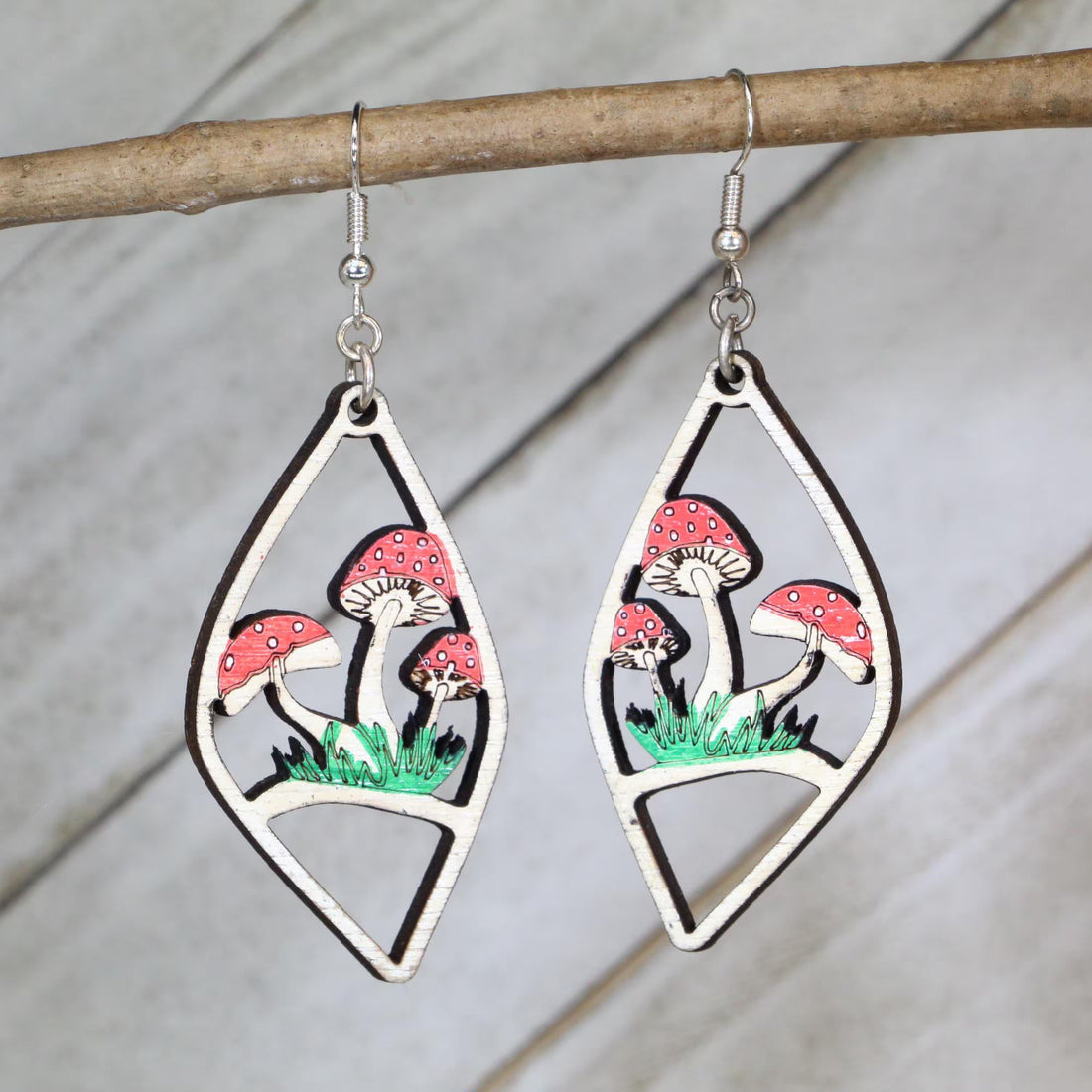 Hand-painted red mushroom woodland scene wooden dangle earrings in an open geometric frame on hypoallergenic .925 sterling silver hooks. Lightweight cottagecore nature jewelry for mushroom lovers, forest enthusiasts, fairy garden fans, and whimsical woodland style.