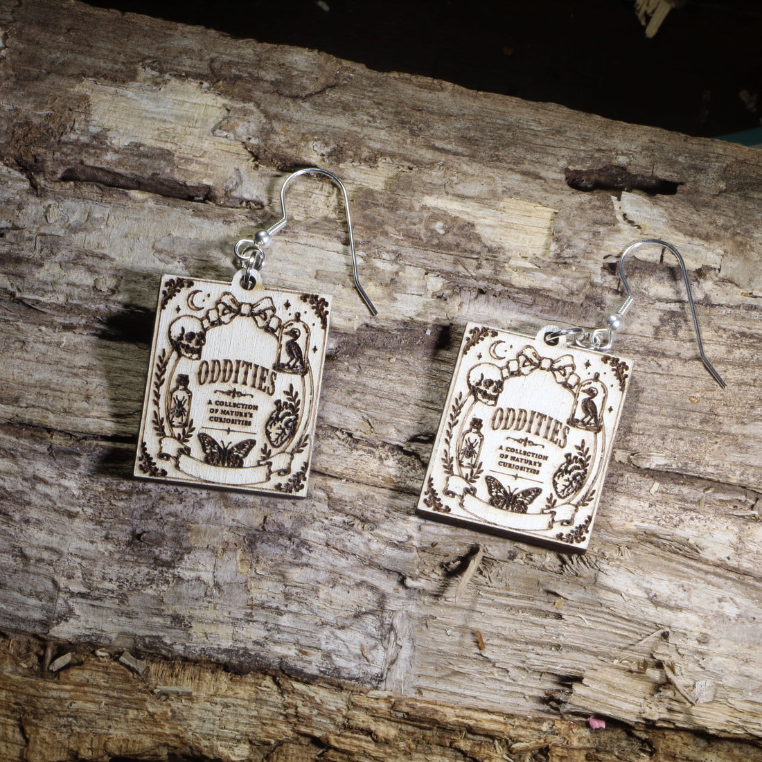 Hand-painted wooden Oddities book cover dangle earrings featuring a vintage-inspired gothic curiosity book cover design on hypoallergenic .925 sterling silver hooks. Lightweight literary jewelry for oddities collectors, gothic decor lovers, horror readers, curiosity cabinet enthusiasts, librarians, and fans of dark, vintage-inspired art.