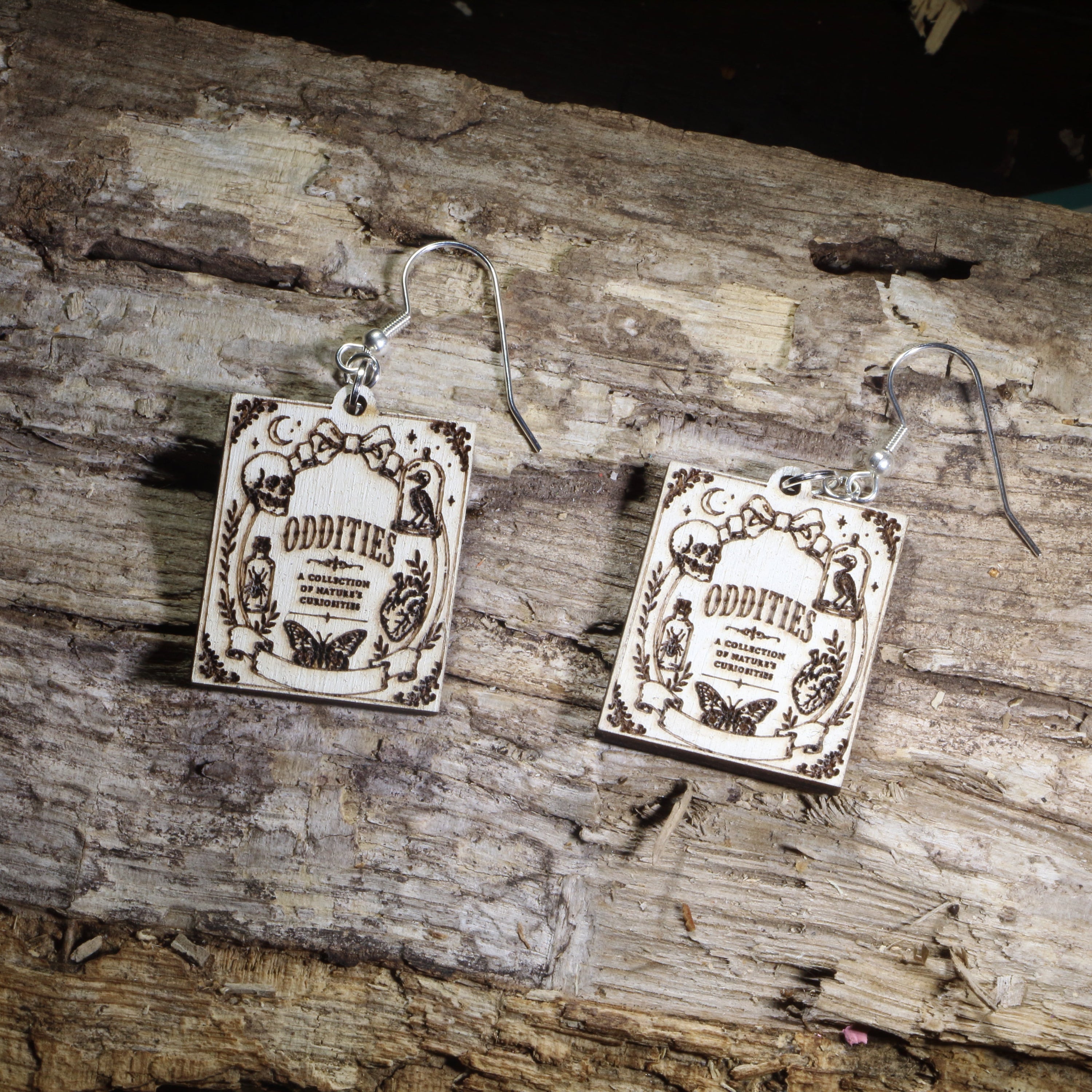 Hand-painted wooden Oddities book cover dangle earrings featuring a vintage-inspired gothic curiosity book cover design on hypoallergenic .925 sterling silver hooks. Lightweight literary jewelry for oddities collectors, gothic decor lovers, horror readers, curiosity cabinet enthusiasts, librarians, and fans of dark, vintage-inspired art.