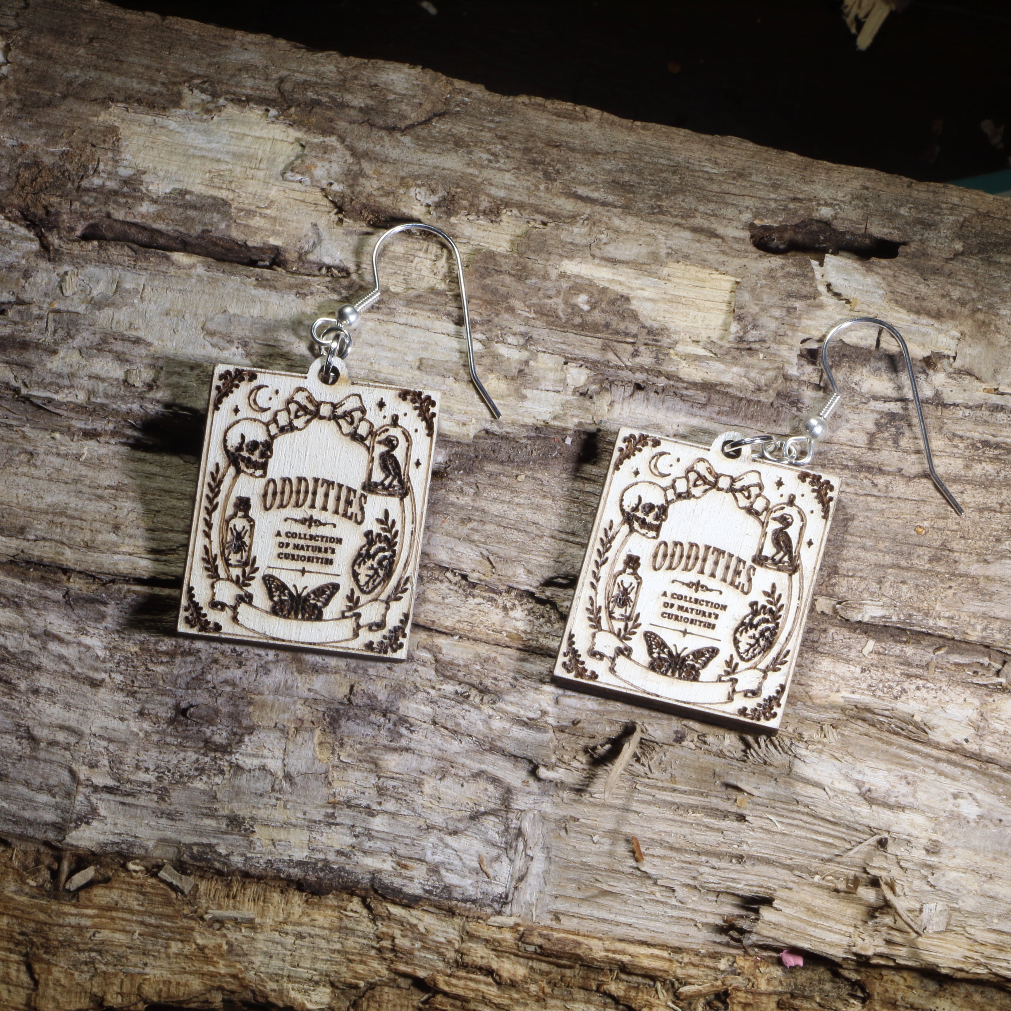Hand-painted wooden Oddities book cover dangle earrings featuring a vintage-inspired gothic curiosity book cover design on hypoallergenic .925 sterling silver hooks. Lightweight literary jewelry for oddities collectors, gothic decor lovers, horror readers, curiosity cabinet enthusiasts, librarians, and fans of dark, vintage-inspired art.