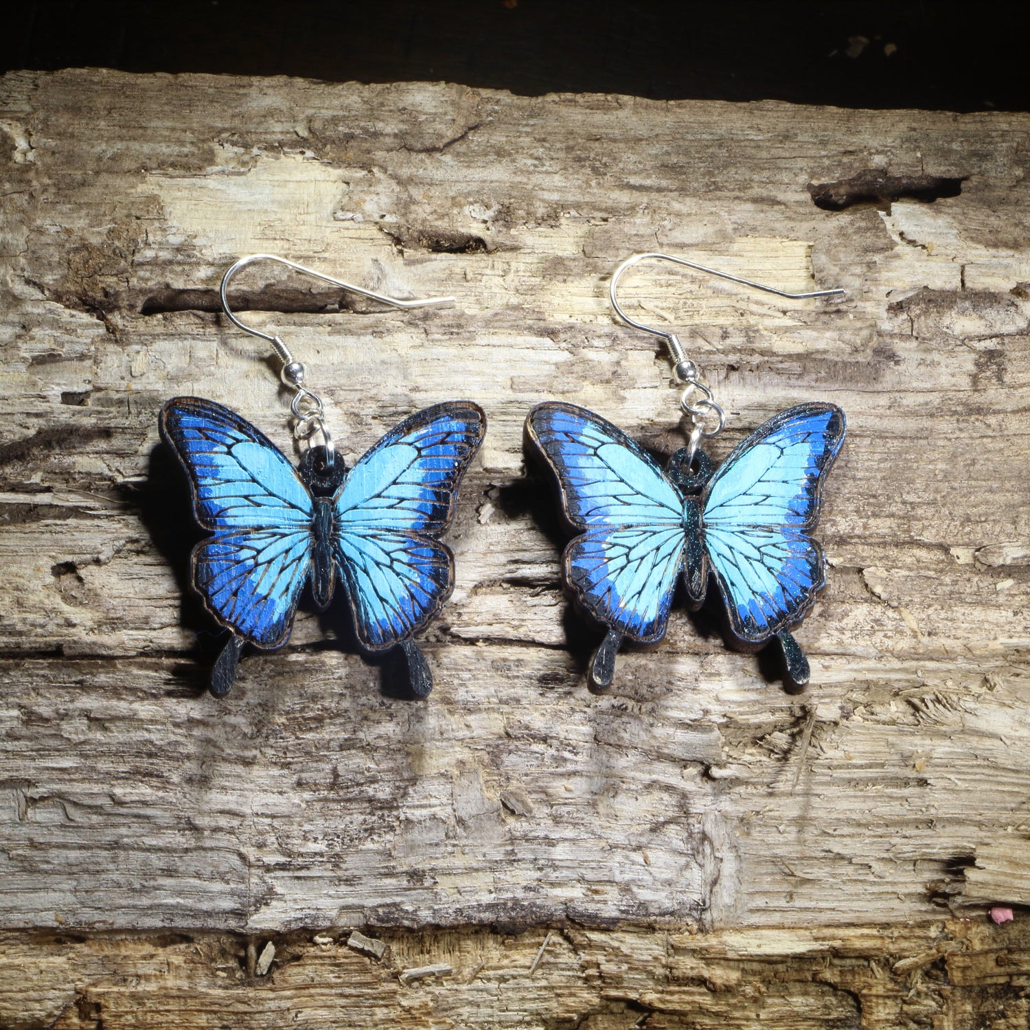 Hand-painted wooden blue morpho butterfly dangle earrings featuring vibrant blue butterfly wings with realistic black edging on hypoallergenic .925 sterling silver hooks. Lightweight butterfly jewelry for nature lovers, gardeners, butterfly enthusiasts, pollinator supporters, and anyone who loves colorful insect-inspired accessories.