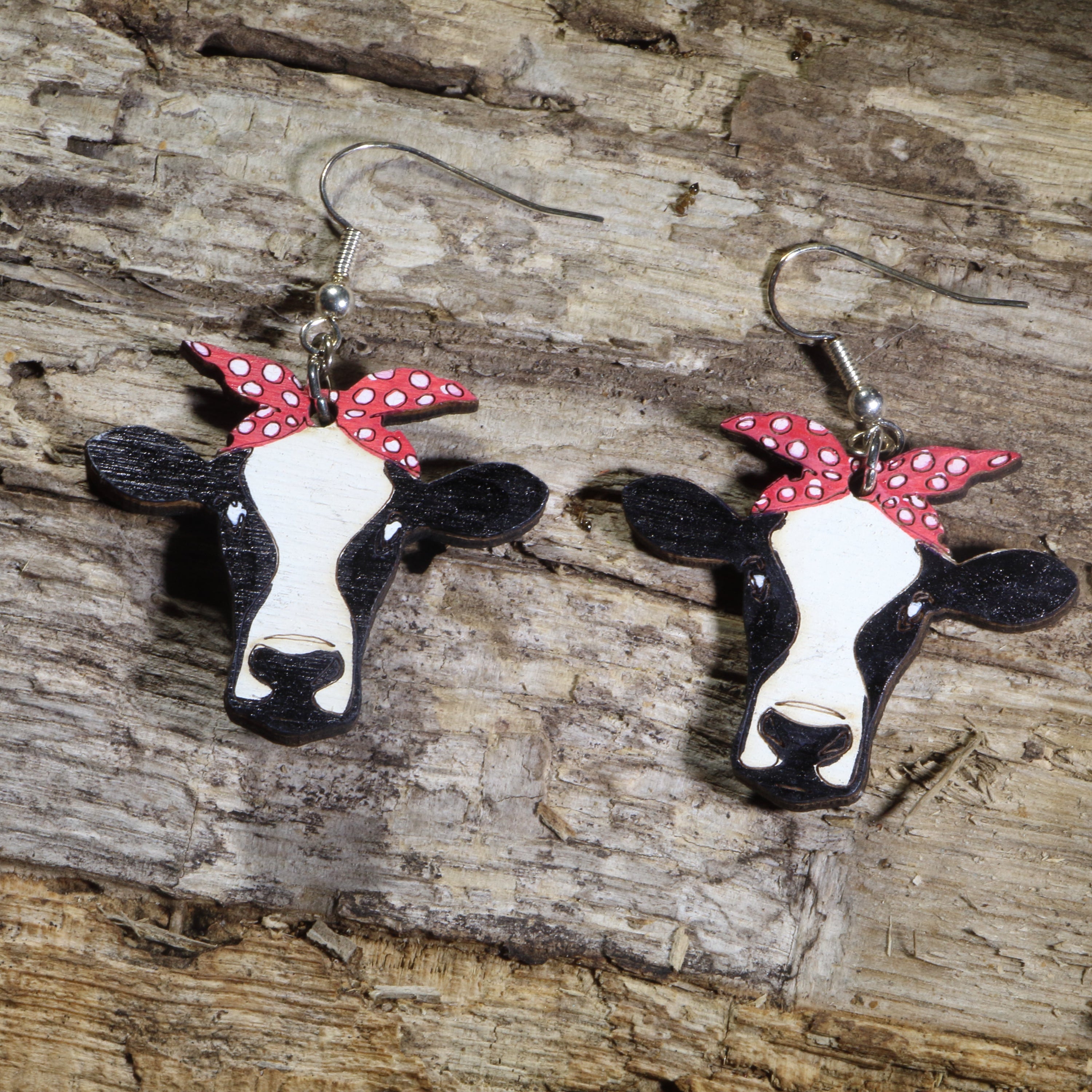 Hand-painted wooden cow head dangle earrings featuring black and white cow faces with red polka dot bandanas on hypoallergenic .925 sterling silver hooks. Lightweight farm animal jewelry perfect for cow lovers, ranch life, country style, and western fashion.