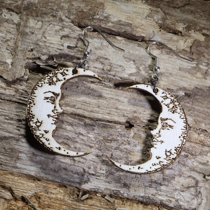 Hand-painted wooden crescent moon dangle earrings featuring engraved vintage moon face details on hypoallergenic .925 sterling silver hooks. Lightweight celestial jewelry perfect for moon lovers, astrology enthusiasts, witchy style, gothic fashion, and lunar-inspired accessories.