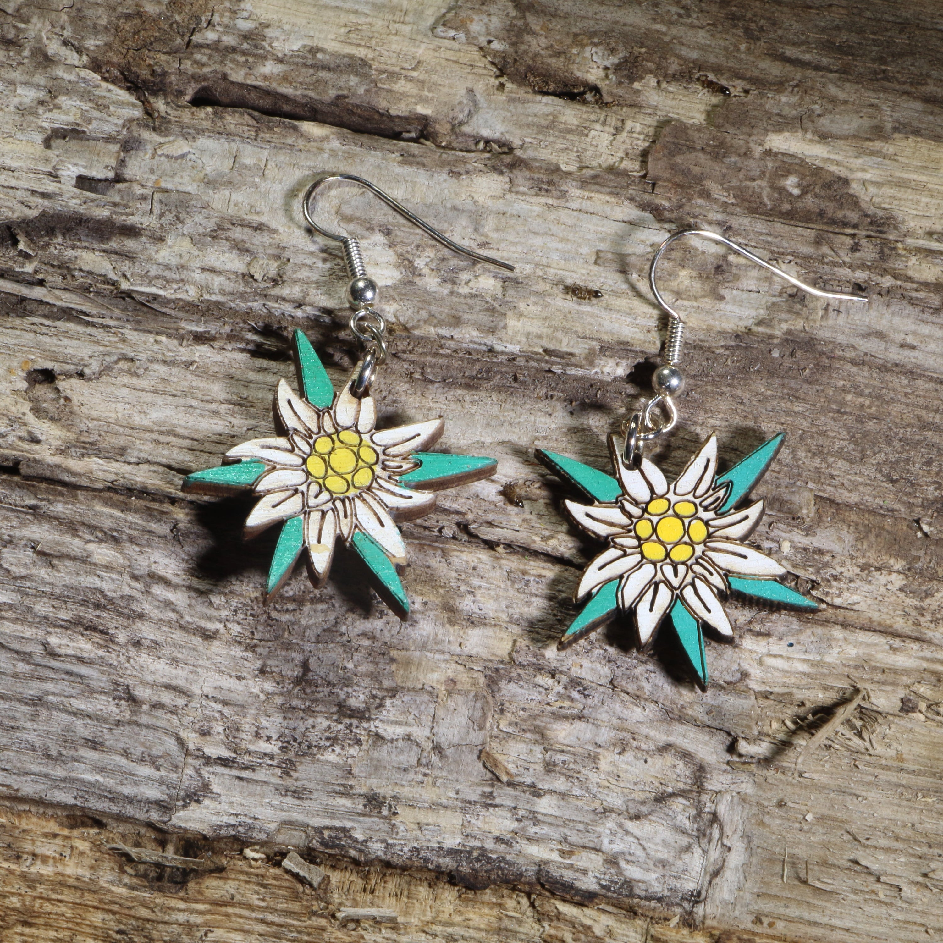Hand-painted wooden edelweiss flower dangle earrings featuring white alpine blossoms with yellow centers and teal accents on hypoallergenic .925 sterling silver hooks. Lightweight floral jewelry perfect for nature lovers, hikers, alpine flower enthusiasts, Swiss and Austrian heritage, and botanical-inspired accessories.