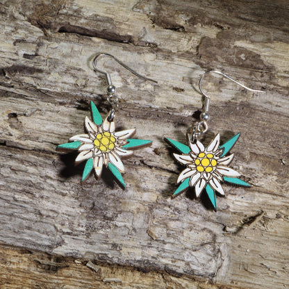 Hand-painted wooden edelweiss flower dangle earrings featuring white alpine blossoms with yellow centers and teal accents on hypoallergenic .925 sterling silver hooks. Lightweight floral jewelry perfect for nature lovers, hikers, alpine flower enthusiasts, Swiss and Austrian heritage, and botanical-inspired accessories.