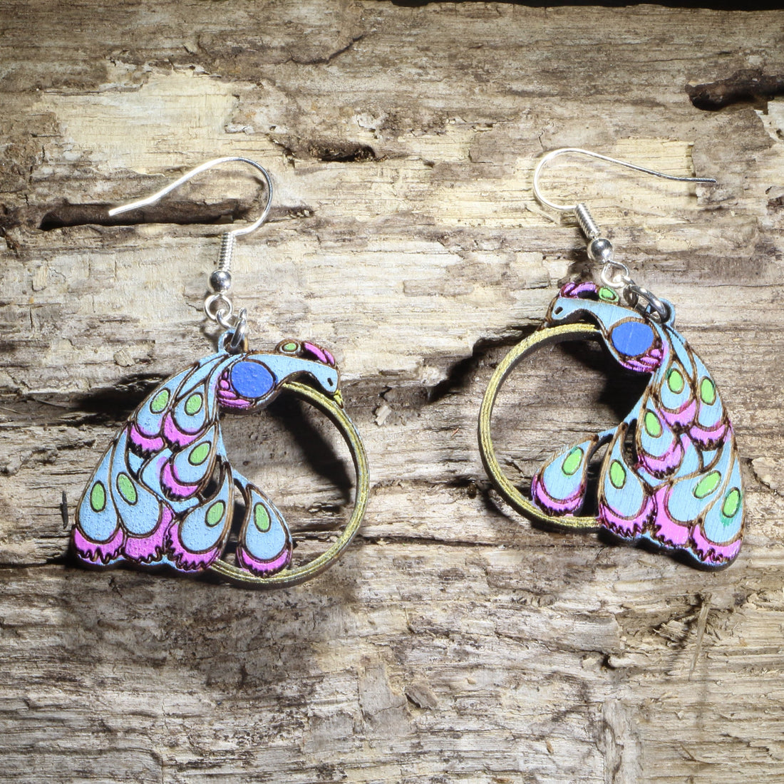 Hand-painted wooden peacock dangle earrings featuring a colorful stylized peacock with vibrant blue, purple, and green feathers and an open circular tail design on hypoallergenic .925 sterling silver hooks. Lightweight bird jewelry for peacock lovers, birdwatchers, nature enthusiasts, and fans of colorful statement accessories.