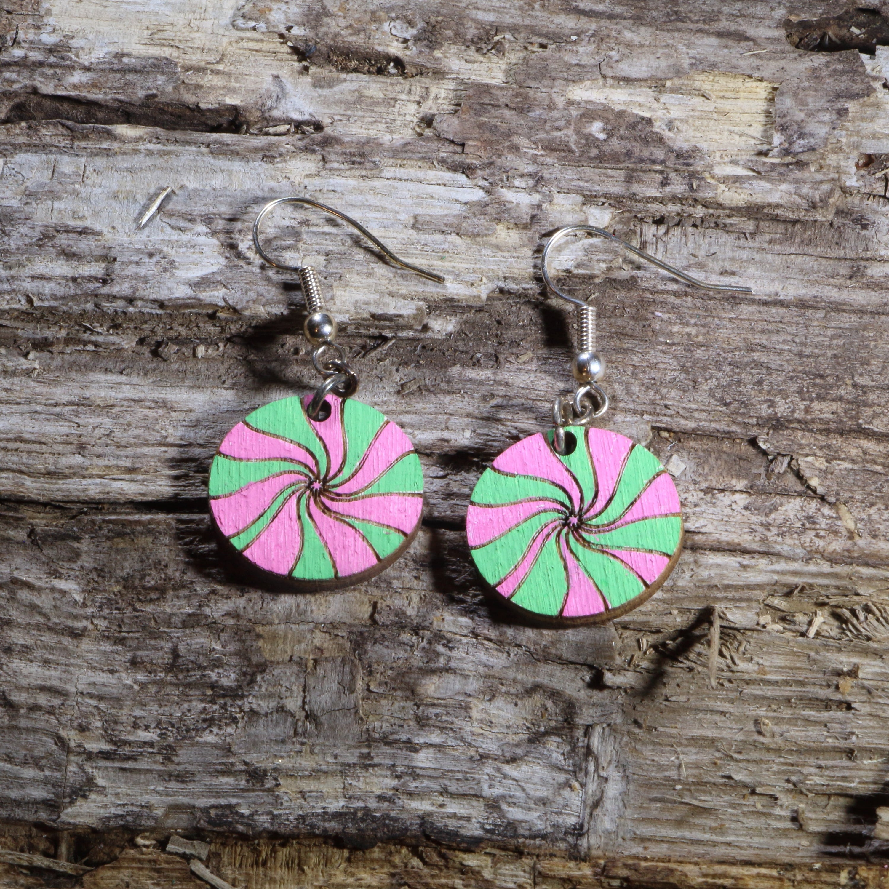 Hand-painted wooden pink and green peppermint candy dangle earrings featuring festive swirled Christmas candies in bright holiday colors. Lightweight Christmas earrings with hypoallergenic .925 sterling silver hooks, perfect for holiday parties, candy lovers, winter celebrations, stocking stuffers, and cheerful festive outfits.