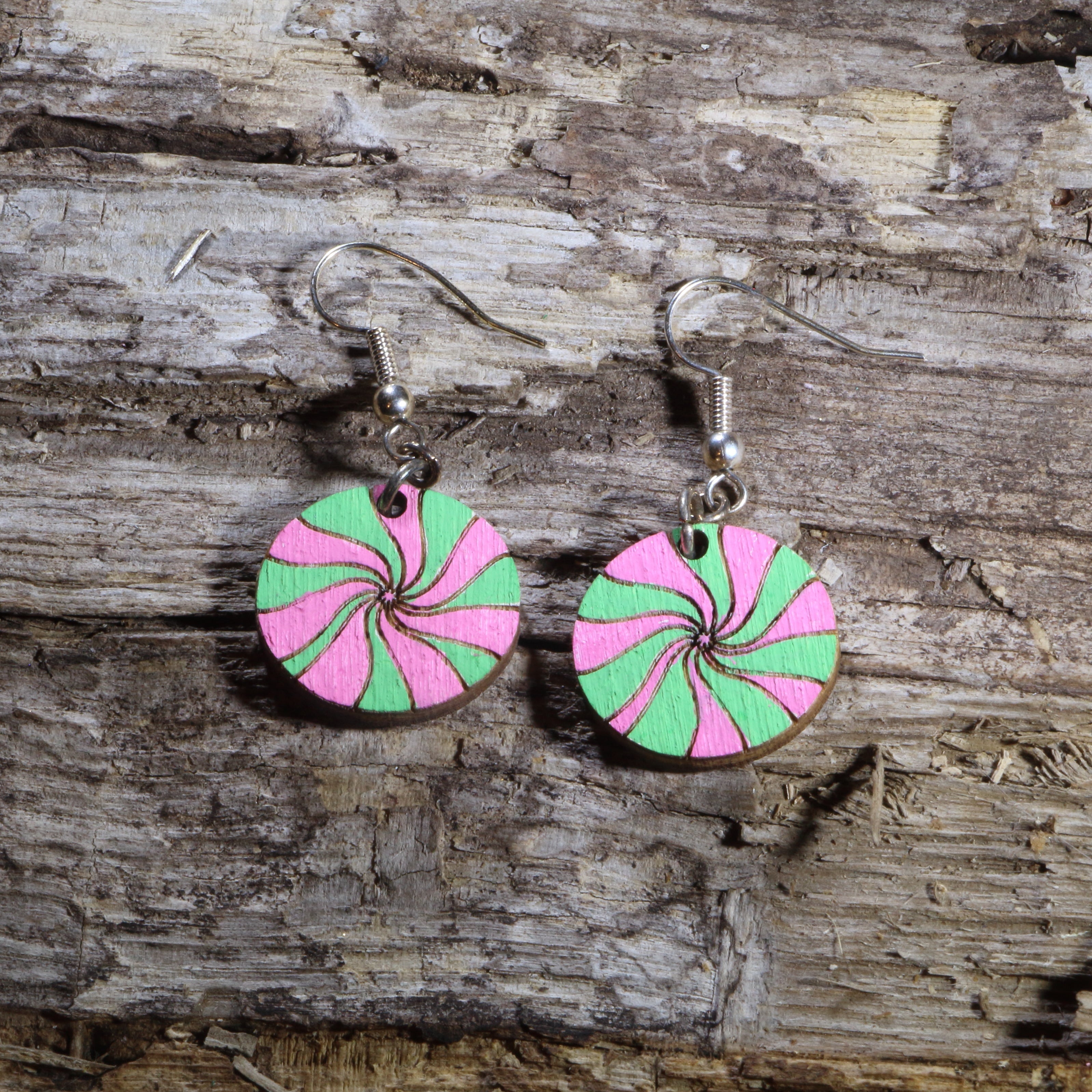 Hand-painted wooden pink and green peppermint candy dangle earrings featuring festive swirled Christmas candies in bright holiday colors. Lightweight Christmas earrings with hypoallergenic .925 sterling silver hooks, perfect for holiday parties, candy lovers, winter celebrations, stocking stuffers, and cheerful festive outfits.