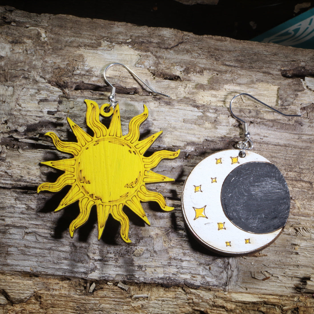 Hand-painted wooden sun and moon mismatched dangle earrings featuring a bright golden sun and a crescent moon with stars on hypoallergenic .925 sterling silver hooks. Lightweight celestial jewelry for astronomy lovers, astrology enthusiasts, witches, pagans, moon gazers, and fans of cosmic-inspired accessories.