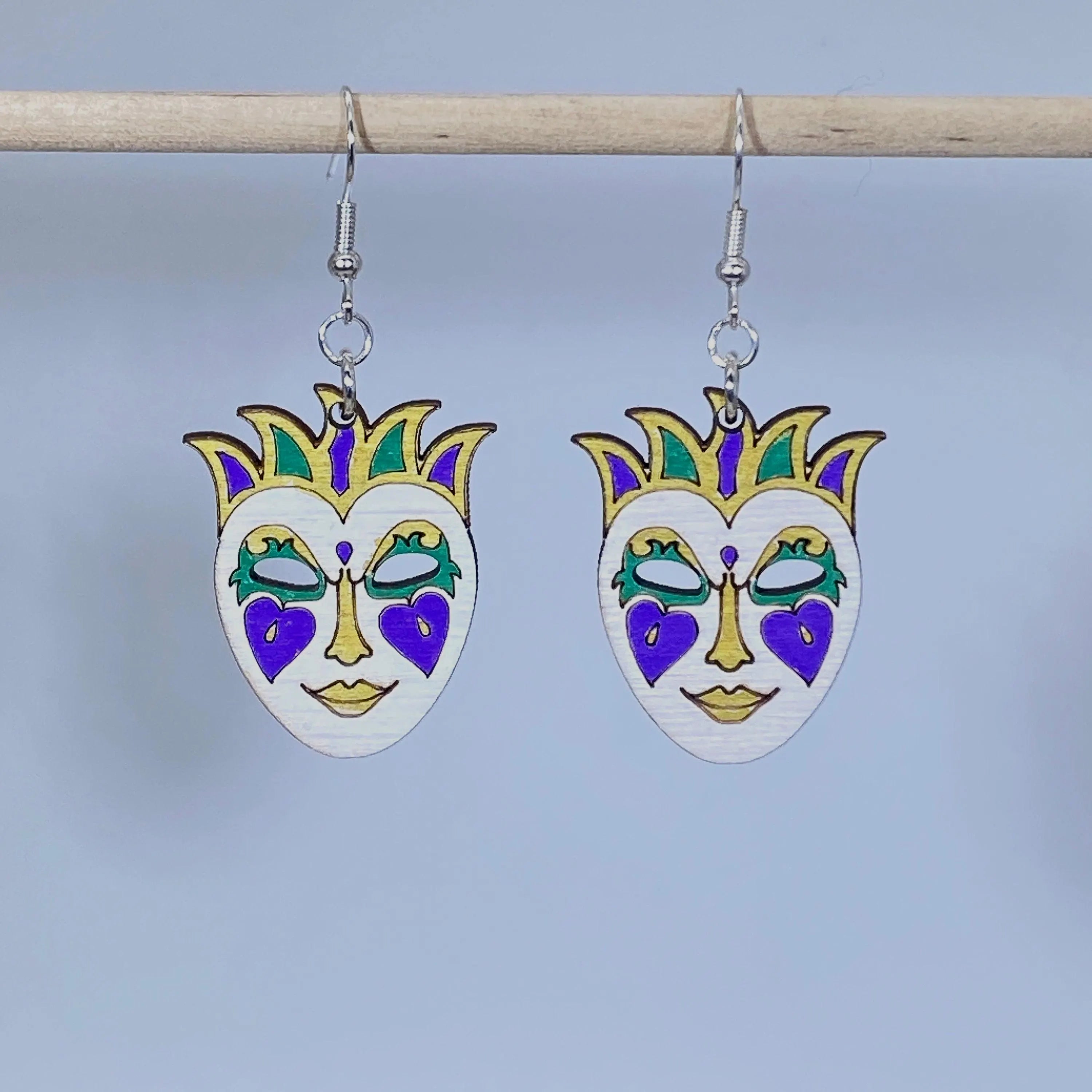 Handcrafted Mardi Gras mask wooden dangle earrings featuring a festive masquerade mask in traditional purple, green, gold, and white colors. Lightweight laser-cut wooden earrings with hypoallergenic .925 sterling silver hooks, perfect for Mardi Gras celebrations, New Orleans festivals, carnival parties, masquerade costumes, Louisiana gifts, and handmade festival jewelry.