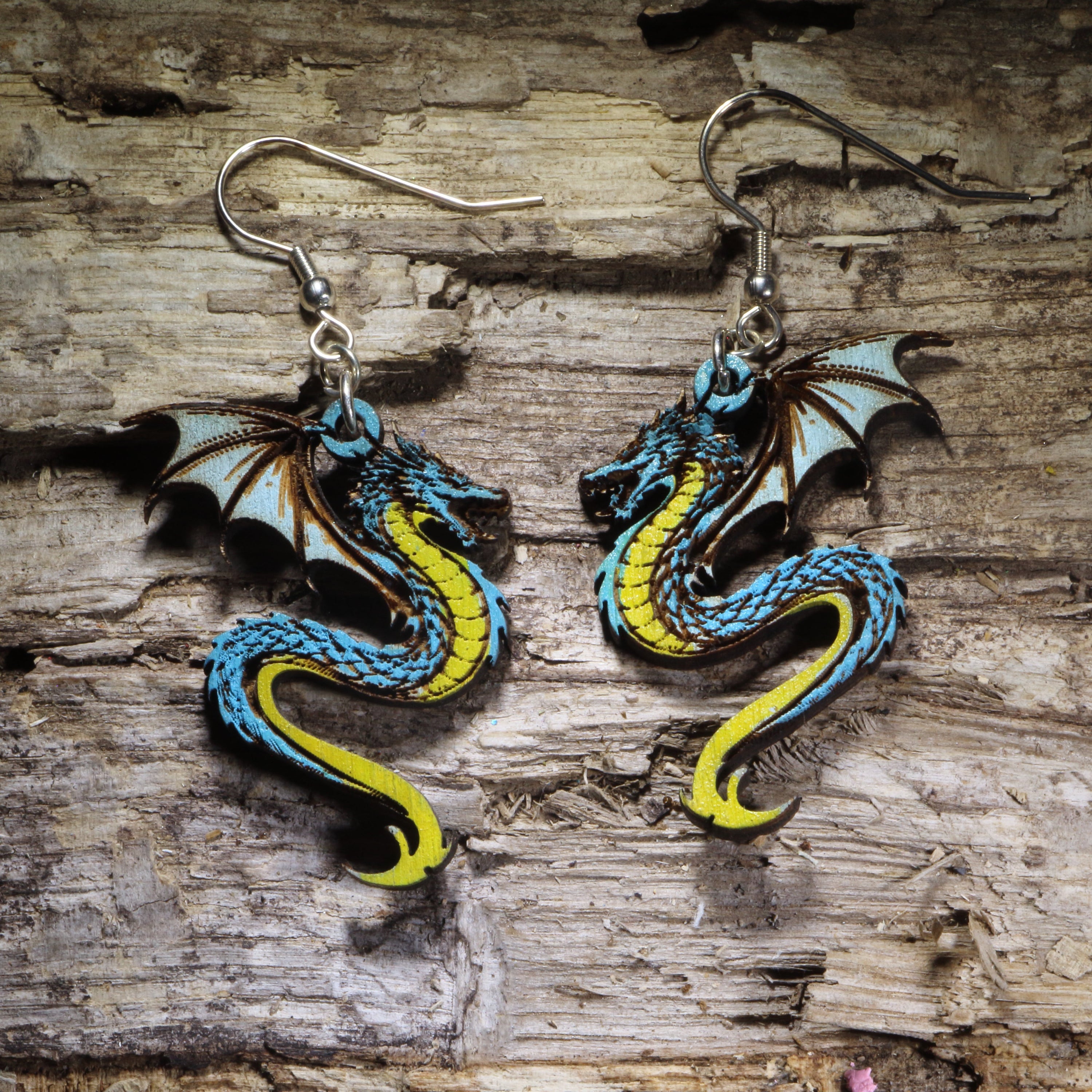 Handcrafted blue dragon wooden dangle earrings featuring a detailed hand-painted fantasy dragon with blue scales, yellow underbelly, and outstretched wings. Lightweightfeaturing a detailed hand-painted fantasy dragon with blue scales, yellow underbelly, and outstretched wings. Lightweight laser-cut wooden earrings with hypoallergenic .925 sterling silver hooks, perfect for dragon lovers, fantasy fans, Dungeons &amp; Dragons players, Renaissance fairs, mythical creature enthusiasts, and handmade fantasy jewelry.