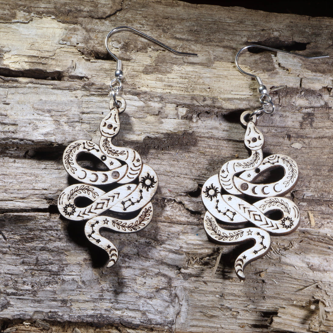 Handcrafted celestial snake wooden dangle earrings featuring engraved moon phases, stars, constellations, and botanical details. Lightweight wooden serpent earrings with hypoallergenic .925 sterling silver hooks, perfect for witchy jewelry lovers, celestial fashion, gothic style, and nature-inspired accessories.