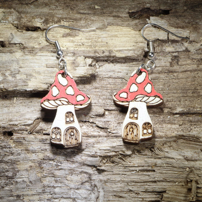 Handcrafted fairy mushroom house wooden dangle earrings featuring whimsical red spotted mushroom cottages with tiny windows and doors. Lightweight hand-painted wooden earrings with hypoallergenic .925 sterling silver hooks, perfect for cottagecore fashion, fairy garden lovers, fantasy enthusiasts, woodland décor fans, whimsical gifts, and enchanted forest accessories.