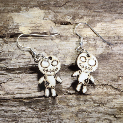 Handmade wooden voodoo doll dangle earrings featuring a stitched rag doll design with oversized eyes and patch details. Lightweight gothic-inspired earrings crafted from wood with hypoallergenic .925 sterling silver hooks, perfect for Halloween, spooky style, horror fans, gothic fashion, and lovers of creepy cute jewelry.