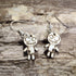 Handmade wooden voodoo doll dangle earrings featuring a stitched rag doll design with oversized eyes and patch details. Lightweight gothic-inspired earrings crafted from wood with hypoallergenic .925 sterling silver hooks, perfect for Halloween, spooky style, horror fans, gothic fashion, and lovers of creepy cute jewelry.