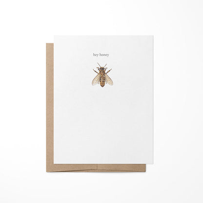A greeting card with a kraft envelope featuring a watercolor painting of a honeybee on the front, placed against a white background.