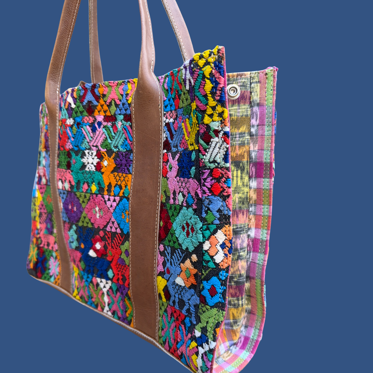 Colorful embroidered bag with brown handles on a blue background