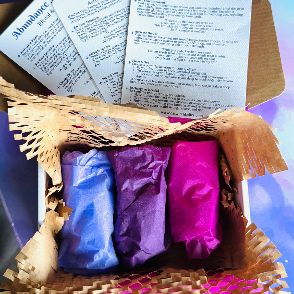 A gift box containing three wrapped spell jars in blue, purple, and pink, with printed cards titled &