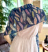 Mannequin wearing a white dress with a blue feather-patterned shawl in a room setting.
