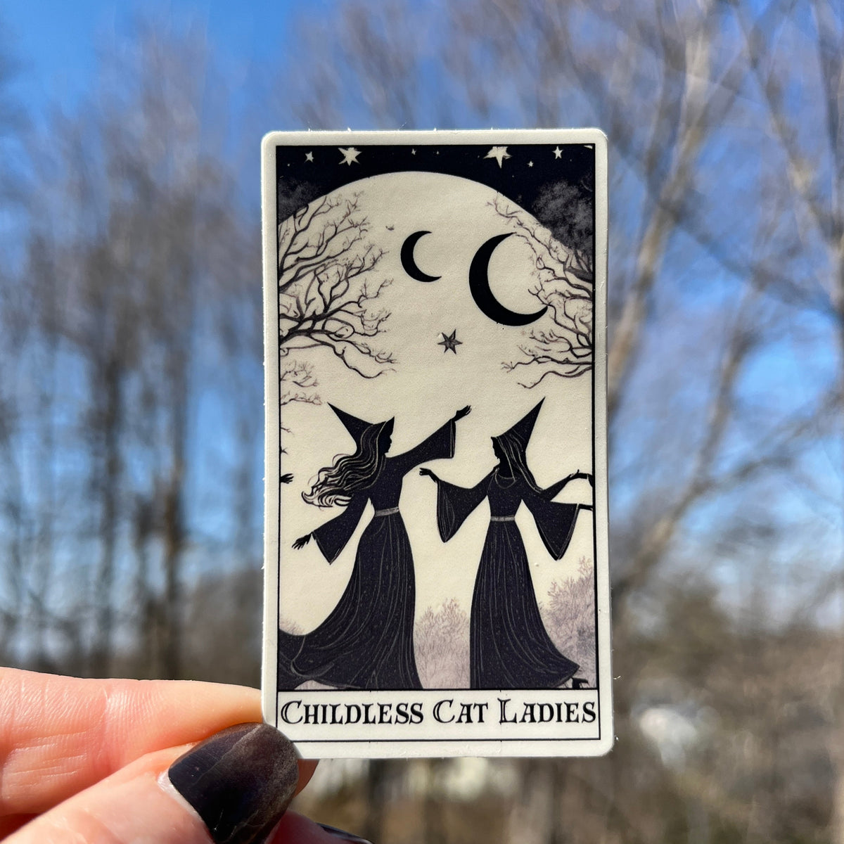 A hand with dark nail polish holds a tarot card titled &