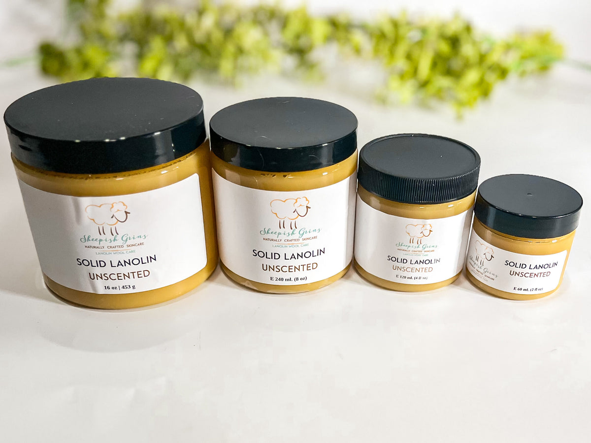 4 jars of lanolin are shown with greenery in the background. The jars are from Sheepish Grins and are arranged from left to right, largest to smallest: 2 oz., 4 oz., 8 oz., and 16 oz