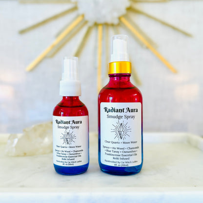 Two red glass spray bottles labeled Radiant Aura Simulflge Spray, one with a white spray top and one with a gold spray top, displayed on a white marble surface with a blurred gold sunburst background.