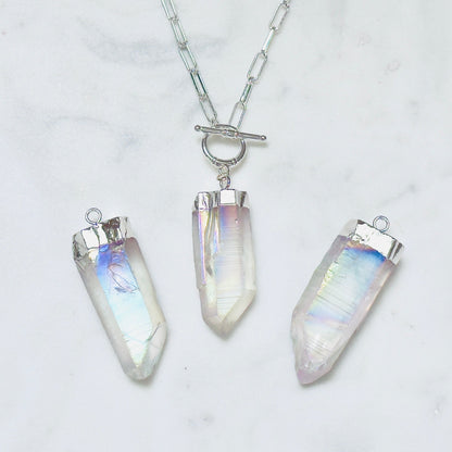 Three silver-toned crystal point pendants on a silver chain, displayed on a white marble surface. The crystals have an iridescent, milky white appearance with subtle pastel rainbow reflections.