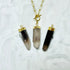Three crystal point pendant necklaces with gold-toned chains and caps, displayed on a white marble surface. The pendants are made from smoky quartz, with one showing a dark smoky top and one showing a lighter smoky top, and a third showing a translucent light gray to smoky gradient.
