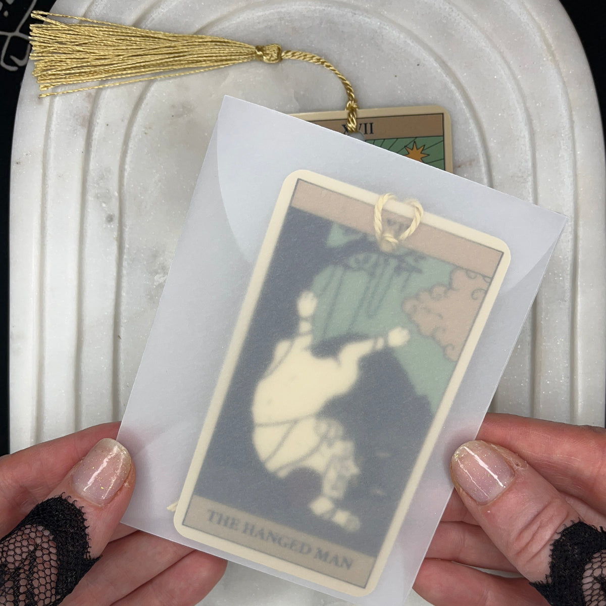 A person holds a tarot card deck in a translucent sleeve, showing the &