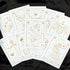 A fan arrangement of white zodiac tarot cards with elegant gold line art and titles including Pisces, Scorpio, Aquarius, and others, displayed on a black fabric background.