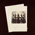 A cream-colored greeting card with a black vintage-style illustration of five witches holding a banner that reads &