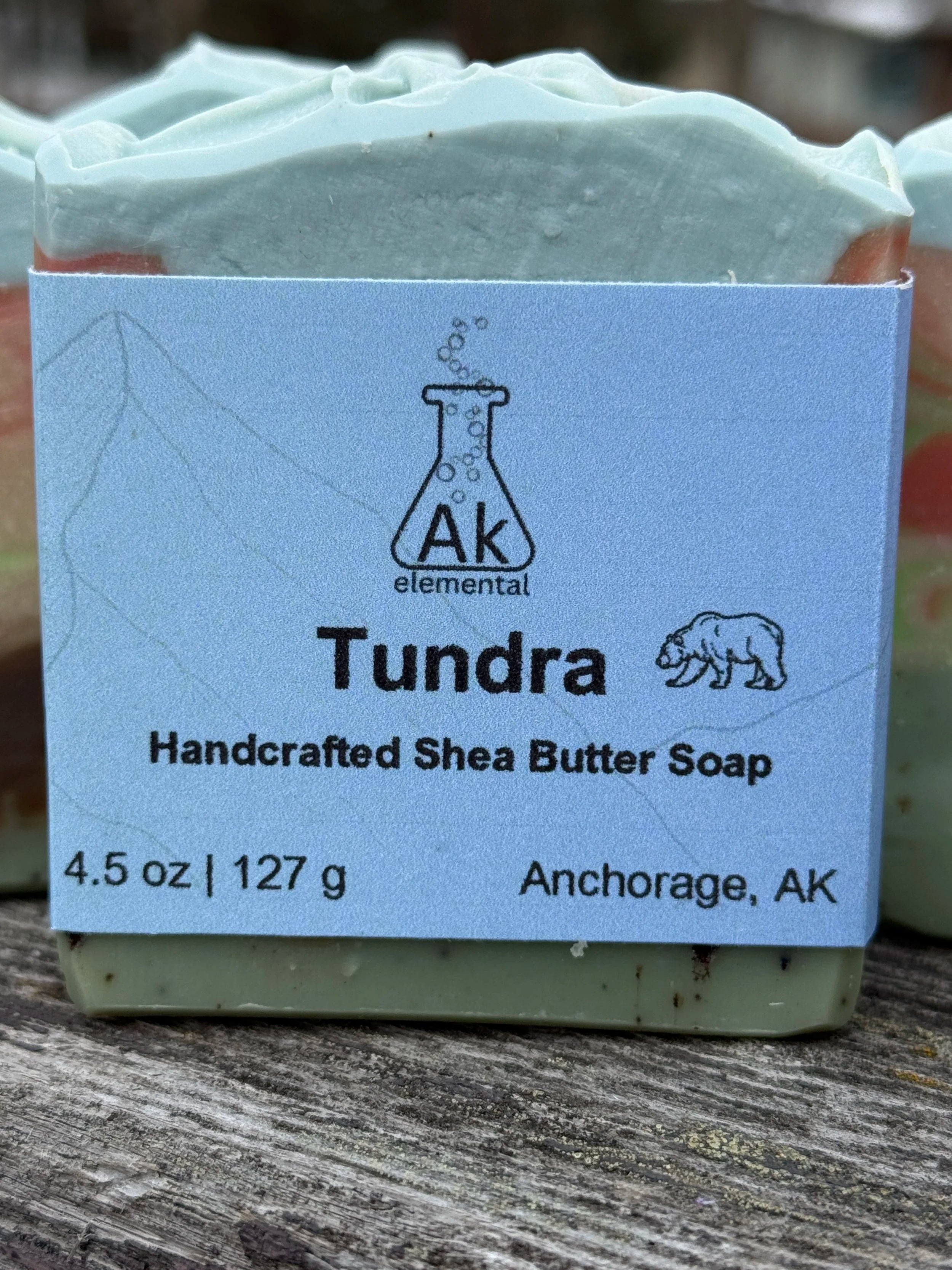 Rectangular soap bar with avocado oil, coconut milk, and bear embed, styled outdoors in snowy Alaska setting