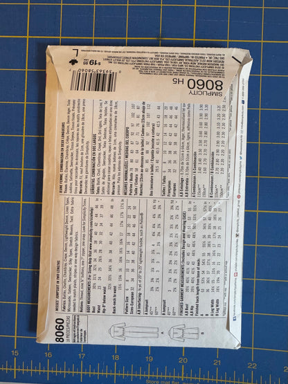 A sewing pattern envelope for Simplicity 8060 H5 is shown flat on a blue cutting mat with yellow grid lines.
