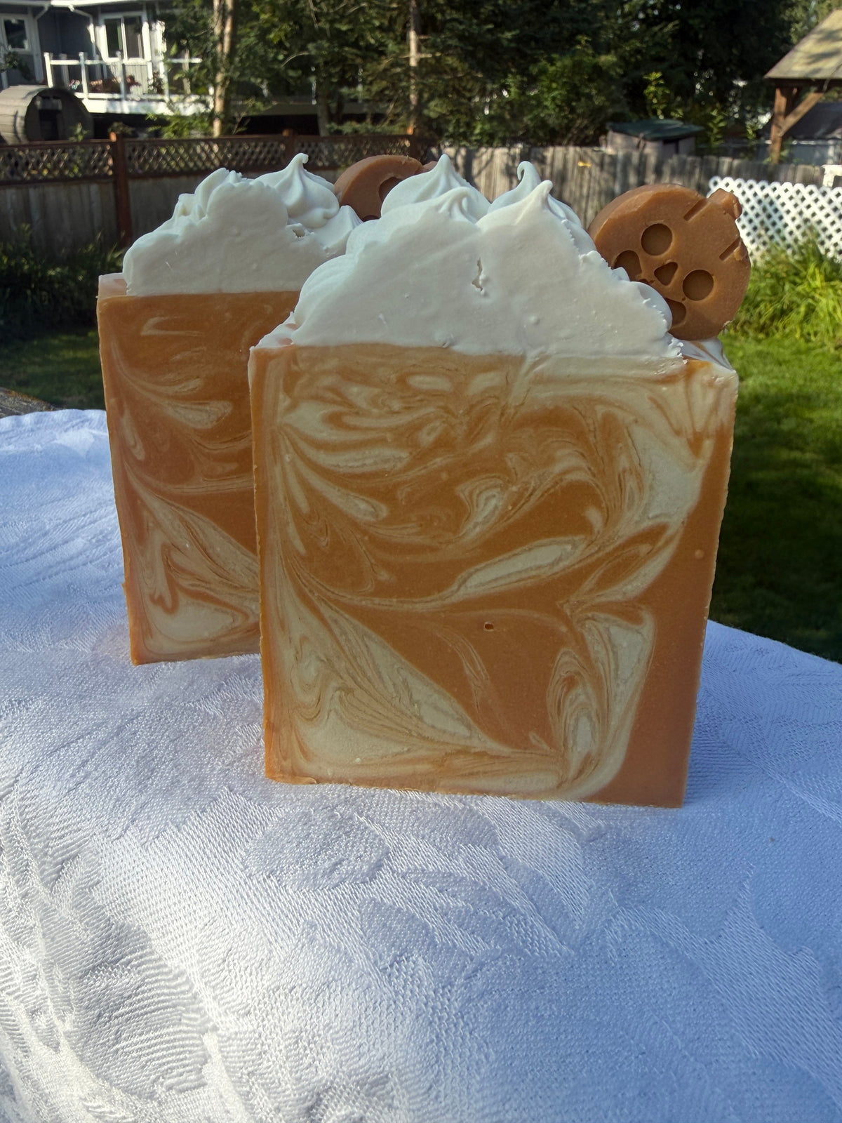 Two Square soap bar with swirls of cream, orange, and warm brown, sitting on a white cloth.