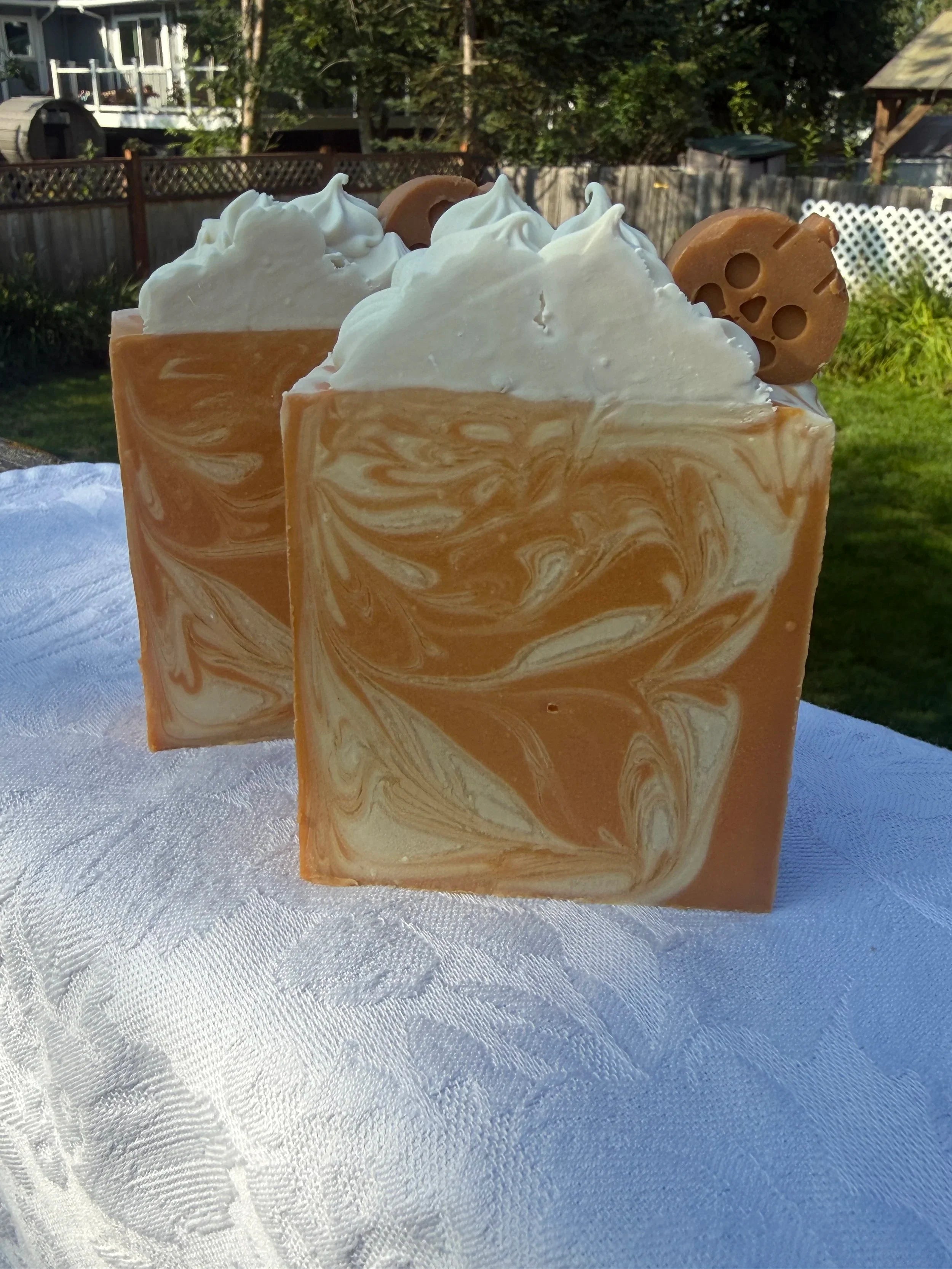 Two Square soap bar with swirls of cream, orange, and warm brown, sitting on a white cloth.
